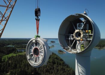 A crane lifting a wind turbine Description automatically generated